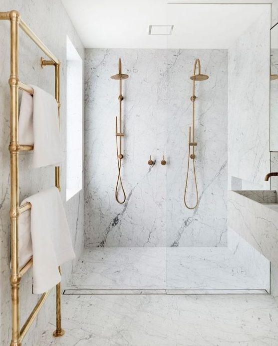 a chic and elegant bathroom done in white marble and gold hardware plus a floating sink and vanity