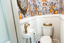 a chic and tiny under the stairs powder room with bold wallpaper and paneling, a wall-mounted sink and a mirror in a vintage frame