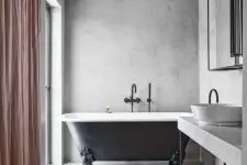 a chic bathroom with concrete walls and a floor, an elegant clawfoot bathtub, a large vainty with a concrete countertop and a pink curtain