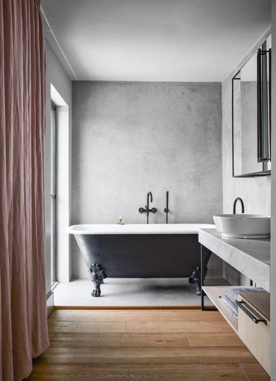 a chic bathroom with concrete walls and a floor, an elegant clawfoot bathtub, a large vainty with a concrete countertop and a pink curtain
