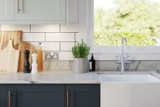 a chic two tone kitchen with light green and graphite grey shaker cabinets, a white subway tile backsplash and white marble countertops