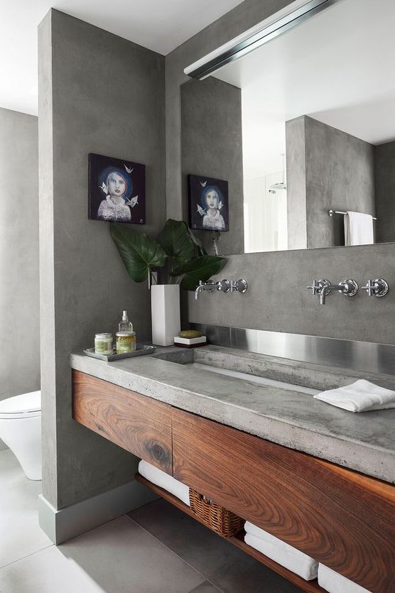 a concrete bathroom with a concrete vanity and wooden storage units, a large mirror and a window to enjoy natural light