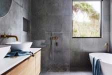 a contemporary bathroom clad with concrete tiles completely, a stained floating vanity, an oval tub, gold fixtures and a bold printed rug