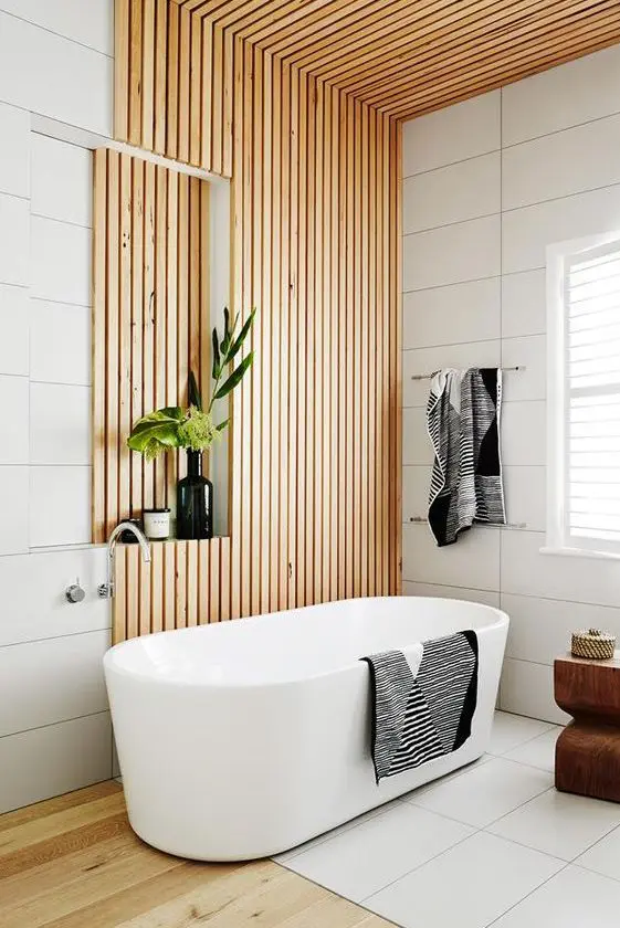 a contemporary bathroom clad with large scale white tiles and wooden slabs, with a hardwood floor, a chic tub and some lovely decor