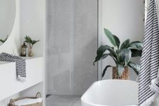 a contemporary bathroom with a concrete wall and floor, an oval bathtub, a sleek vanity and a round mirror plus potted plants