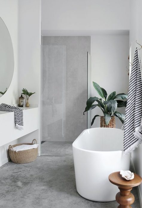 a contemporary bathroom with a concrete wall and floor, an oval bathtub, a sleek vanity and a round mirror plus potted plants