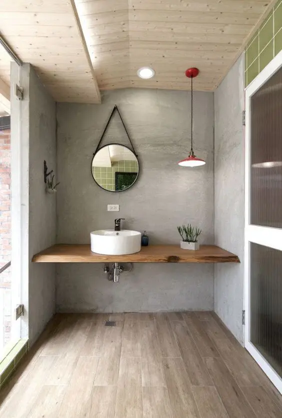 a contemporary bathroom with concrete walls, a light-stained wooden floor, a shelf-like vanity with a round sink and a round mirror