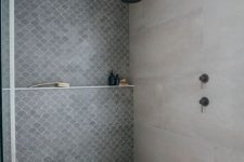 a contemporary shower space with concrete walls and a floor, a grey fish scale tile accent wall and dark fixtures is chic