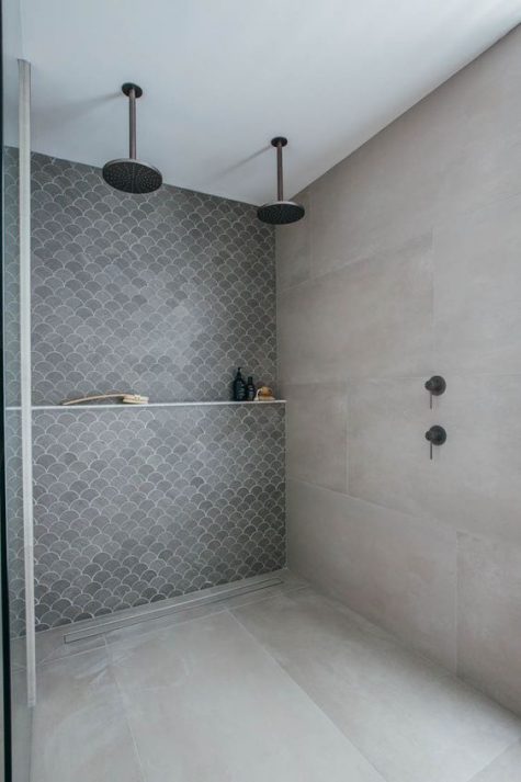 a contemporary shower space with concrete walls and a floor, a grey fish scale tile accent wall and dark fixtures is chic