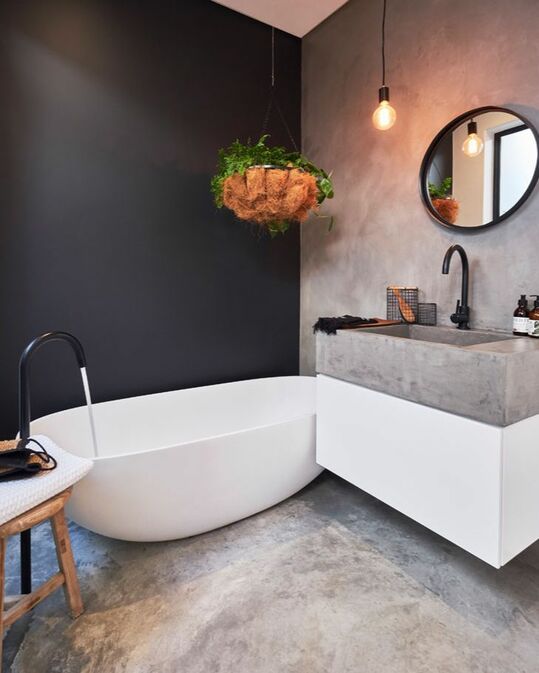 a contrasting bathroom with concrete walls and floor, a black accent wall, a white tub and a concrete sink plus black fixtures