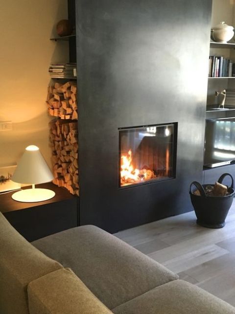 a cozy contemporary space with a fireplace clad with blackened metal, a firewood storage niche and shelves, neutral furniture