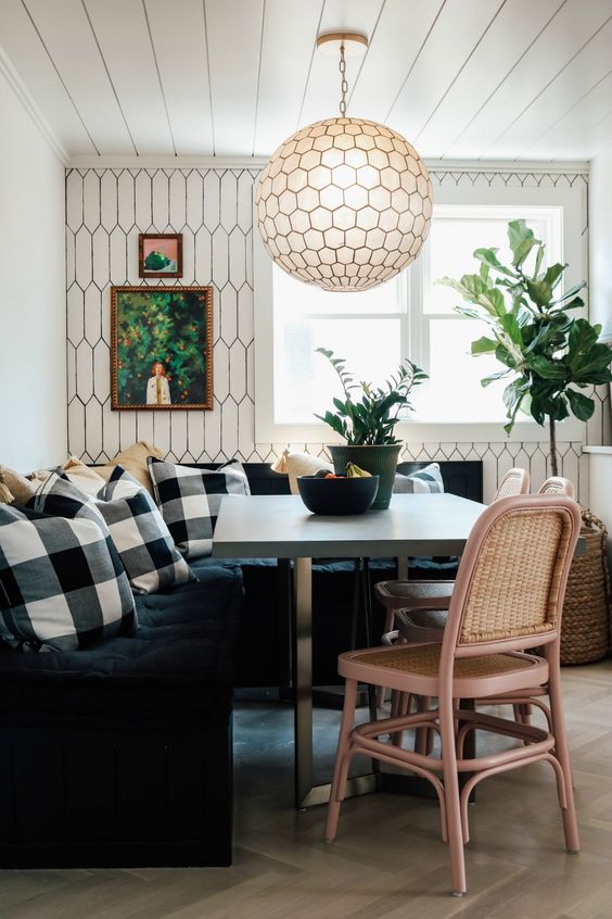 a cozy little dining nook with a black tufted banquette, check pillows, a concrete table, woven chairs and a hexagon pendant lamp