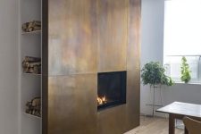 a dining space with an accent feature – a fireplace clad with aged metal sheets and with hidden firewood storage