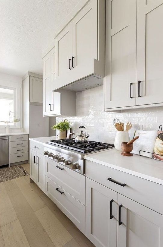 a dreamy and airy neutral kitchen with shaker style cabinets, white tiles and countertops, black handles is a beautiful space to cook in