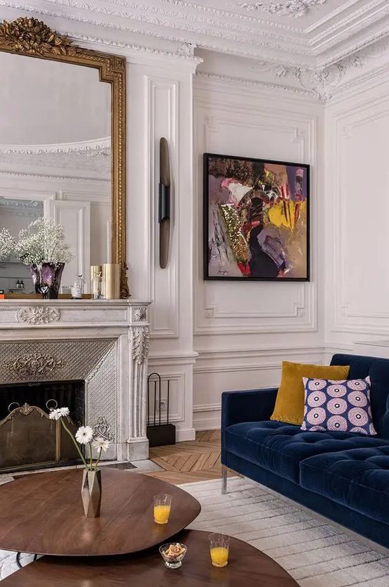 a fantastic Parisian living room with layered ornated molding, with a refined marble fireplace and a large mirror over it, with a navy velvet sofa