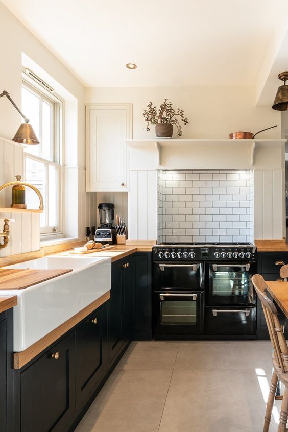 a fantastic bold black and white farmhouse kitchen with shaker cabinets, butcherblock countertops, a white subway tile backsplash and brass touches