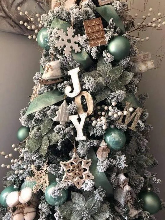 a farmhouse christmas tree decorated with wooden letters, beads, twigs, branches, snowflakes and green ornaments and leaves