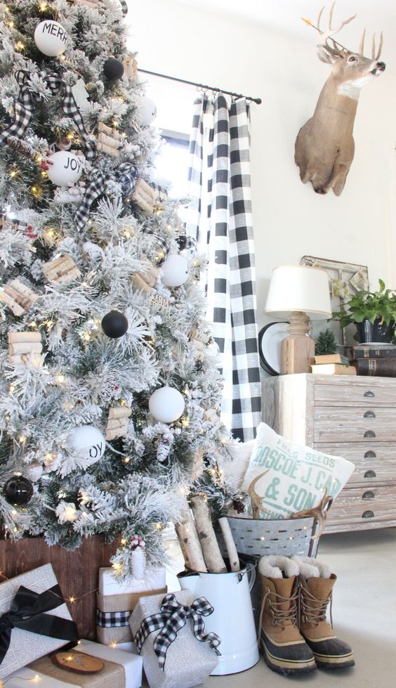 a farmhouse flocked Christmas tree with blakc and white ornaments, mini log ornaments, lights, buffalo check ribbons is cool