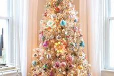 a flocked Christmas tree decorated with lights, colorful and pastel vintage ornaments and a lit up Christmas tree topper