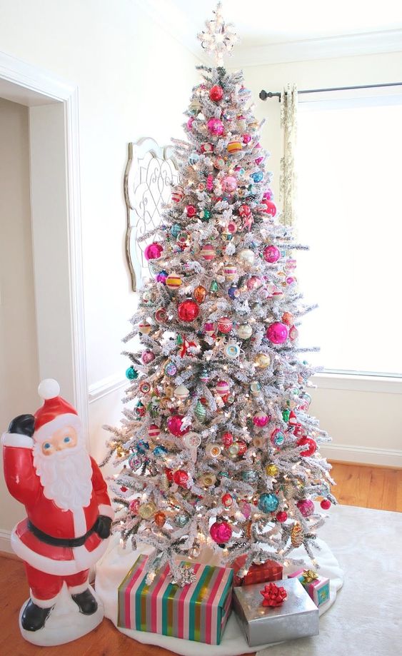 a flocked Christmas tree decorated with red, pink, green, yellow and silver ornaments of various sizes and shapes and spruced up with lights