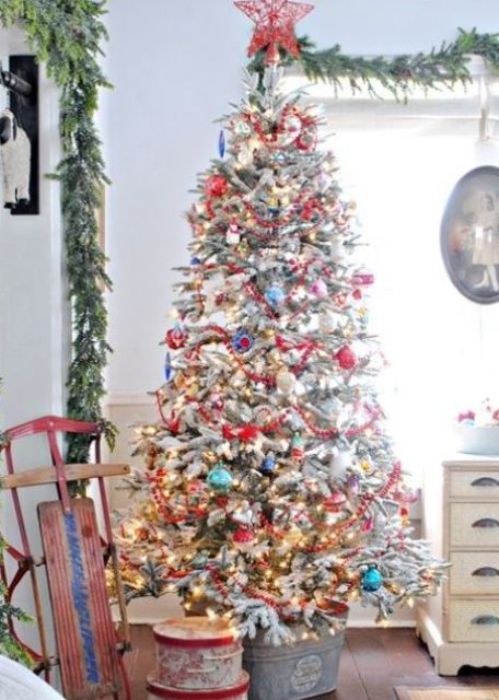 a flocked Christmas tree with colorful ornaments, lights and a red yarn star tree topper looks really vintage like