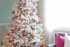 a flocked Christmas tree with lights, colorful ornaments, striped ribbons and frozen branches on the top