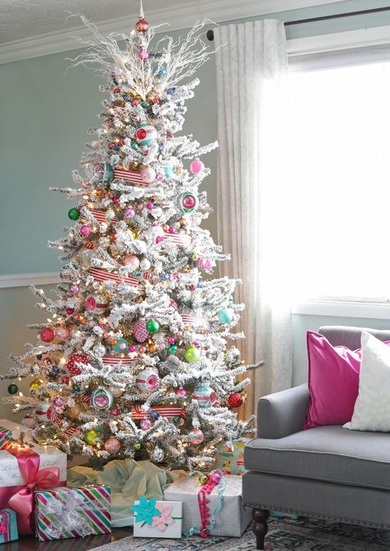 a flocked Christmas tree with lights, colorful ornaments, striped ribbons and frozen branches on the top