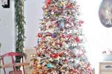 a flocked Christmas tree with red beaded garlands, colorful vintage ornaments and lights and a red yarn star tree topper