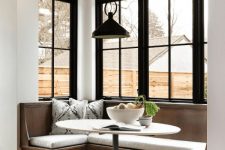 a fresh and natural dining space with a stained wood banquette seating with neutral upholstery, an oval table and a black pendant lamp