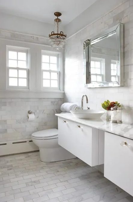 a glam white bathroom done with a floating vanity, white marble tiles and a crystal chandelier