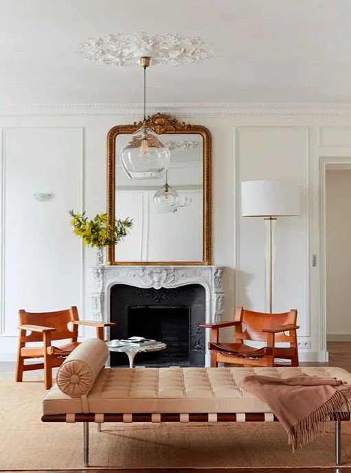 a gorgeous Parisian chic living room with ornated crown modling and a ceiling medallion, with a non-working fireplace, a chic couch and leather chairs