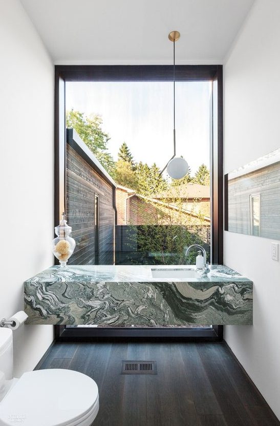 a green marble modern vanity in a small powder room with a view to the courtyard is a gorgeous touch of luxury in the space