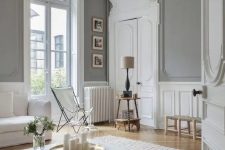 a jaw-dropping neutral Parisian space with grey walls, white wainscoting, crown molding, white furniture and neutral-colored chairs and stools