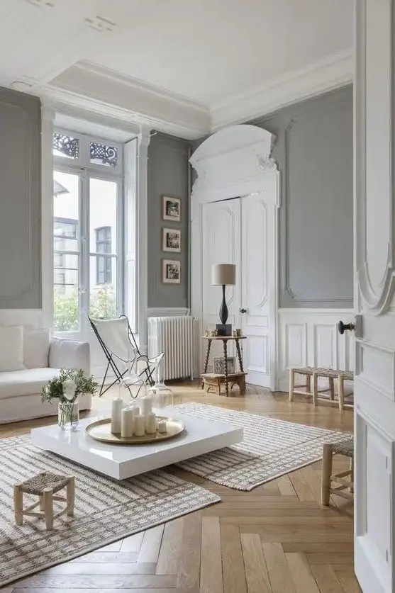 a jaw dropping neutral Parisian space with grey walls, white wainscoting, crown molding, white furniture and neutral colored chairs and stools