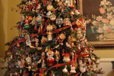 a large Christmas tree decorated with red ribbons, oversized colorful vintage ornaments and some lights is a bold maximalist idea