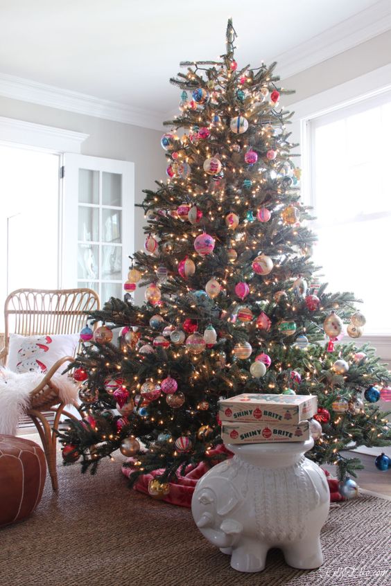 a large Christmas tree decorated with vintage Christmas ornaments and lights and a pink velvet tree skirt