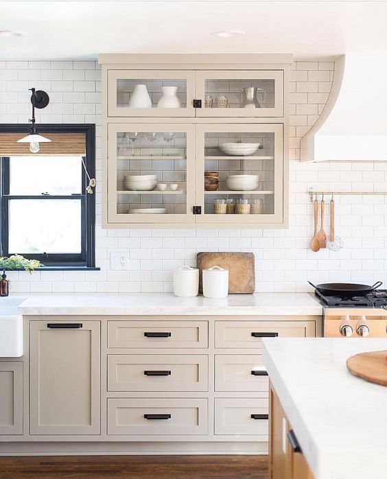 a light-stained farmhouse kitchen with shaker cabinets, black handles, white subway tiles on the backsplash and a navy-framed window