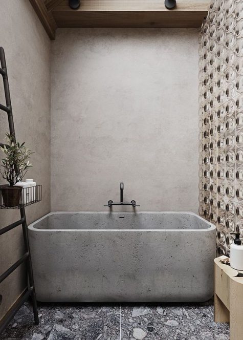 a lovely bathroom of concrete, with a terrazzo floor, a catchy accent wall and a concrete bathtub plus a black ladder