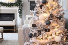 a lovely flocked Christmas tree with lights, black and white ornaments, black wood slice ones, lights and snowy garlands