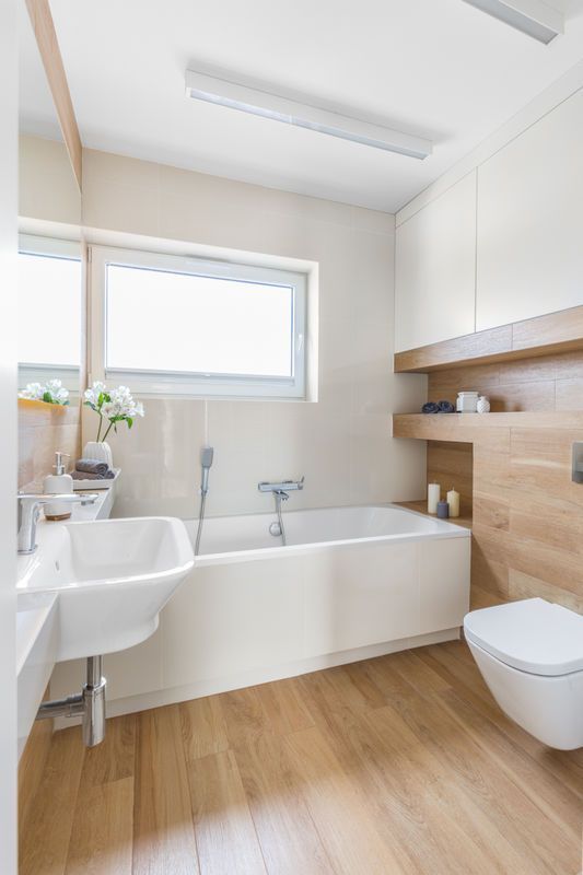 a minimalist bathroom done in neutrals, with a light-stained wood floor and matching shelves, white appliances and a window