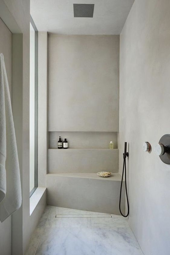 a minimalist bathroom done with neutral concrete, a large window, black fixtures and a marble floor is pure chic