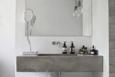 a minimalist bathroom with white plaster walls, a concrete floating sink, a basket with towels and a laconic mirror