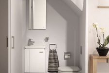 a minimalist under stair powder room done in white, with floating appliances and a rectangular mirror plus a striped towel