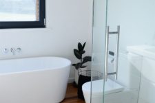 a minimalist white bathroom with a light-stained wood floor, a shower space, an oval tub and some dark touches for more drama