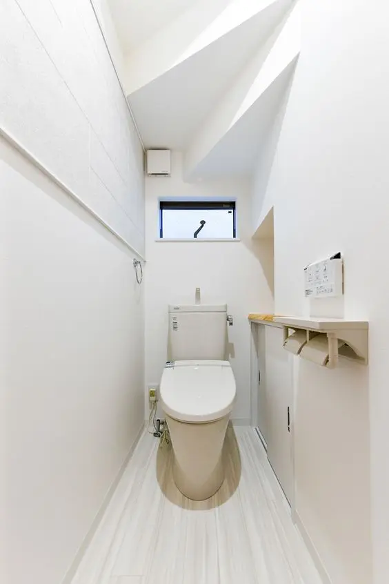a minimalist white under the stairs powder room with a shelf and a toilet plus a window and nothing else