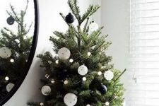 a modern Christmas tree decorated with blak and white ornaments and pompom lights plus an old sweater as a tree skirt