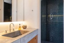 a modern bathroom with a concrete tile floor, a teal tile shower space, a built-in vanity and a thick concrete countertops with a sink