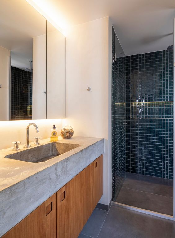 a modern bathroom with a concrete tile floor, a teal tile shower space, a built in vanity and a thick concrete countertops with a sink