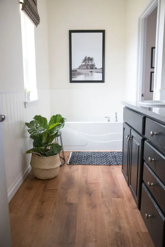 a modern bathroom with white planked walls, a rich-stained wooden floor, a catchy tub and a black vanity, a potted plant for a fresh touch