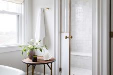 a modern elegant bathroom in neutrals, with a hardwood floor, a large shower space clad with white tiles and a wooden side table